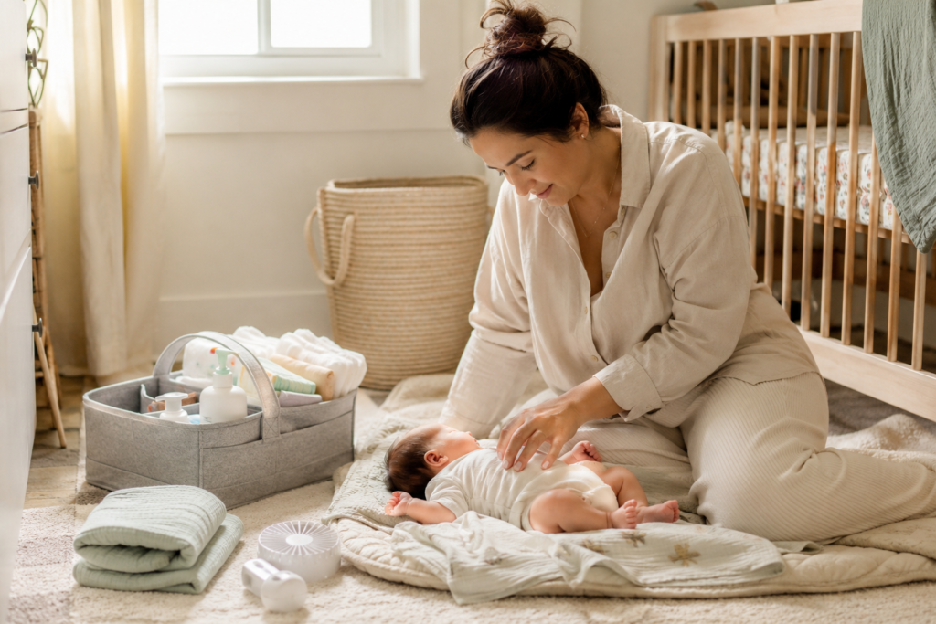Mom sitting on the nursery floor with her baby and everyday newborn essentials nearby.