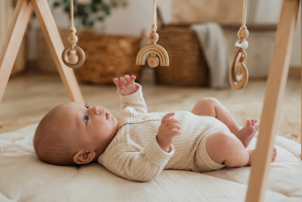 Newborn baby lying under play gym looking at hanging toys